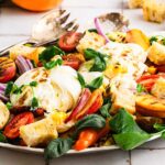 A vibrant peach panzanella salad featuring burrata cheese, ripe tomatoes, juicy peaches, crunchy croutons, and fresh mixed greens elegantly plated on a white dish.
