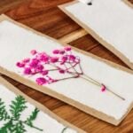 Handmade pressed flower bookmark DIY, featuring pink flowers and green leaves on white paper with a brown paper border.