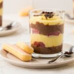Glass of zuppa inglese topped with chocolate shavings on a plate.
