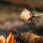 A campfire strawberry on a stick, covered in toasted marshmallow, held over the flames for a sweet treat.