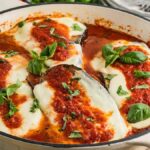 Baked Chicken Sorrentino with tomato sauce, melted cheese, and fresh basil in a white skillet.