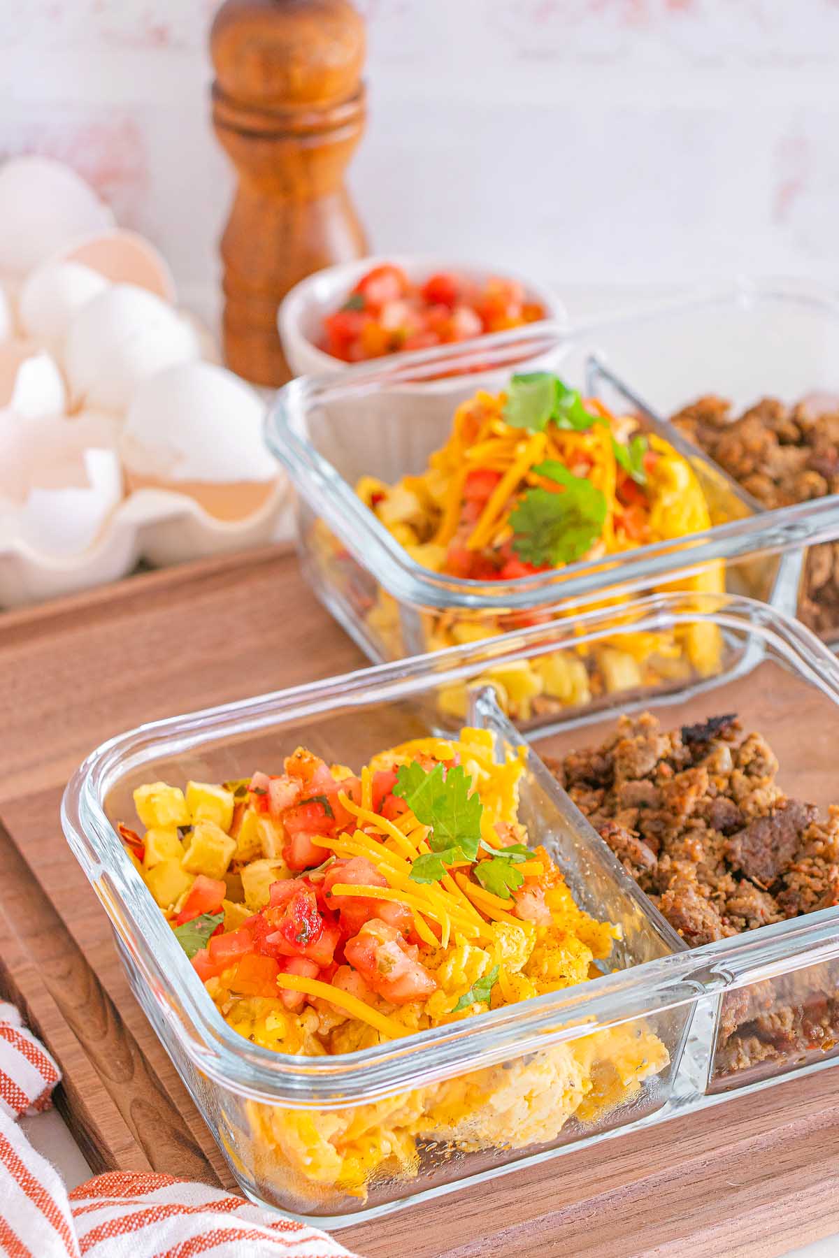 Glass meal prep containers with scrambled eggs, shredded cheese, ground sausage, and fresh salsa on a wooden table—perfect for easy meal prep breakfast taco bowls.