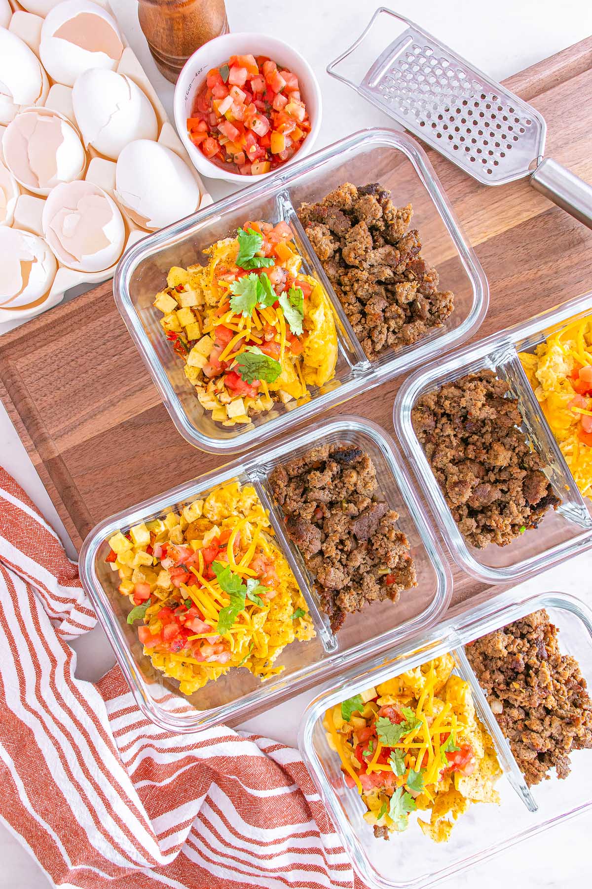 Glass meal prep containers with scrambled eggs, ground meat, cheese, and salsa on a wooden board—perfect for easy meal prep breakfast taco bowls.