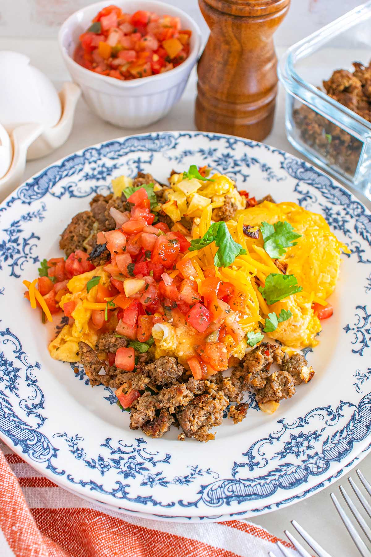 A plate of scrambled eggs, ground meat, shredded cheese, and salsa, garnished with cilantro—these meal prep breakfast taco bowls are a delicious and convenient way to start your day.