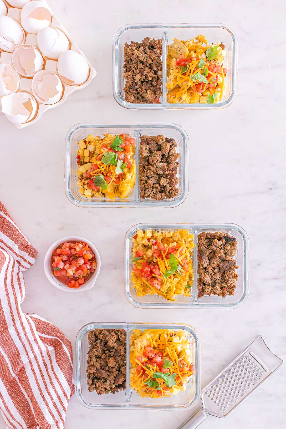 Three glass meal prep containers with scrambled eggs, ground beef, cheese, and salsa on a marble countertop make the perfect meal prep breakfast taco bowls.