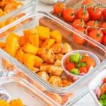 Glass meal prep containers filled with Meal Prep Cajun Chicken and Sweet Potato Bowls, served alongside a fresh cherry tomato salad for a flavorful and convenient meal option.