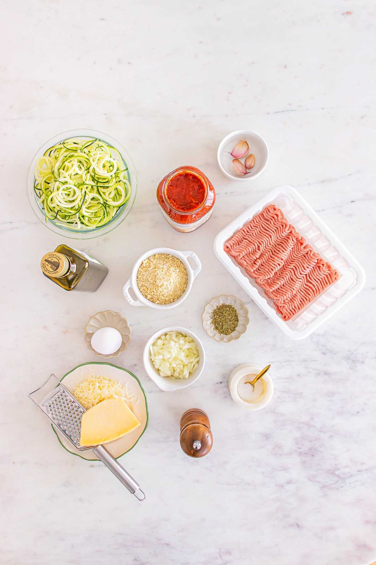 Ingredients for a pasta dish, including Meal Prep Turkey Meatballs & Zoodles, sauce, cheese, egg, and seasonings.