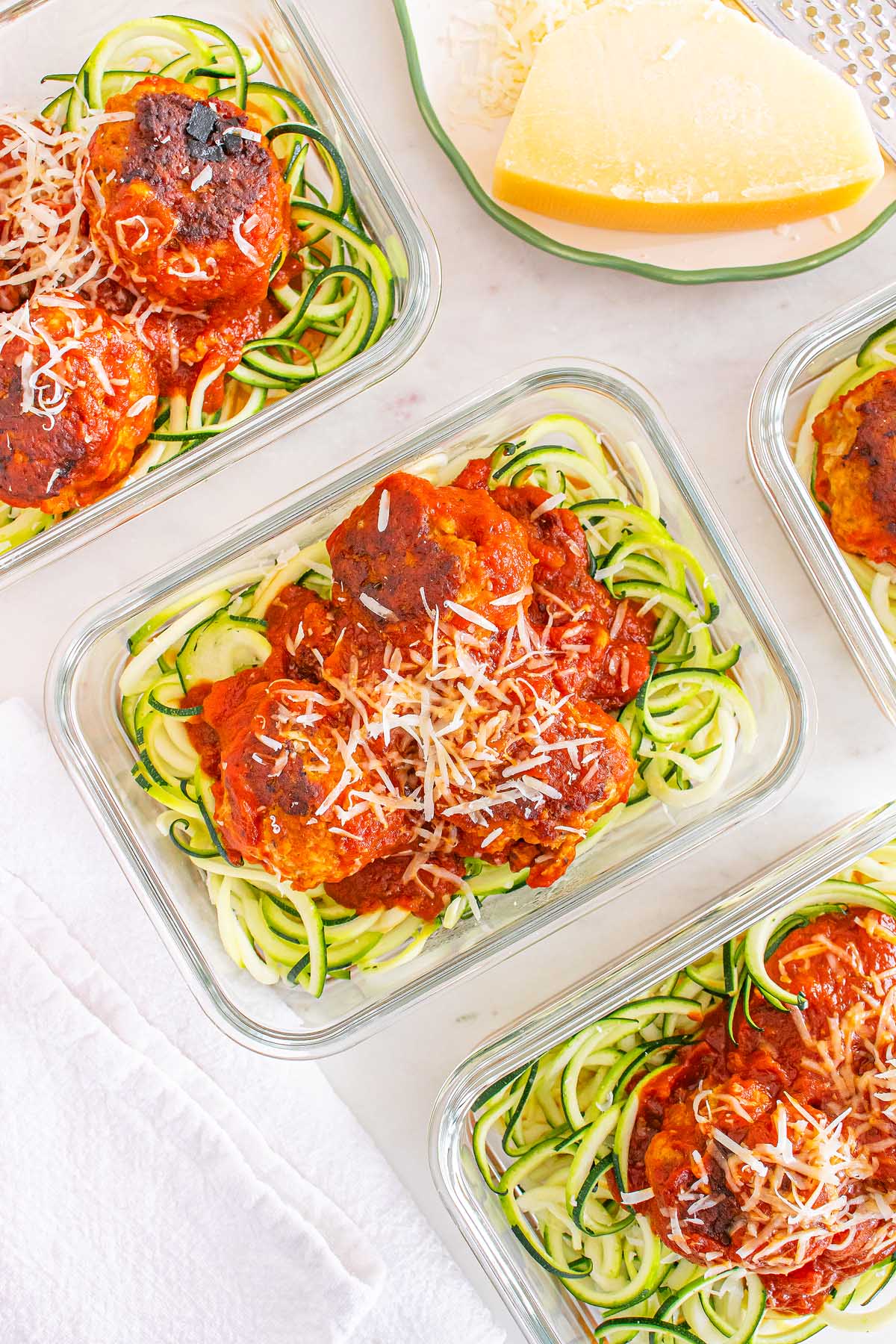 Glass containers filled with Meal Prep Turkey Meatballs & Zoodles, topped with rich tomato sauce and a sprinkle of grated cheese.