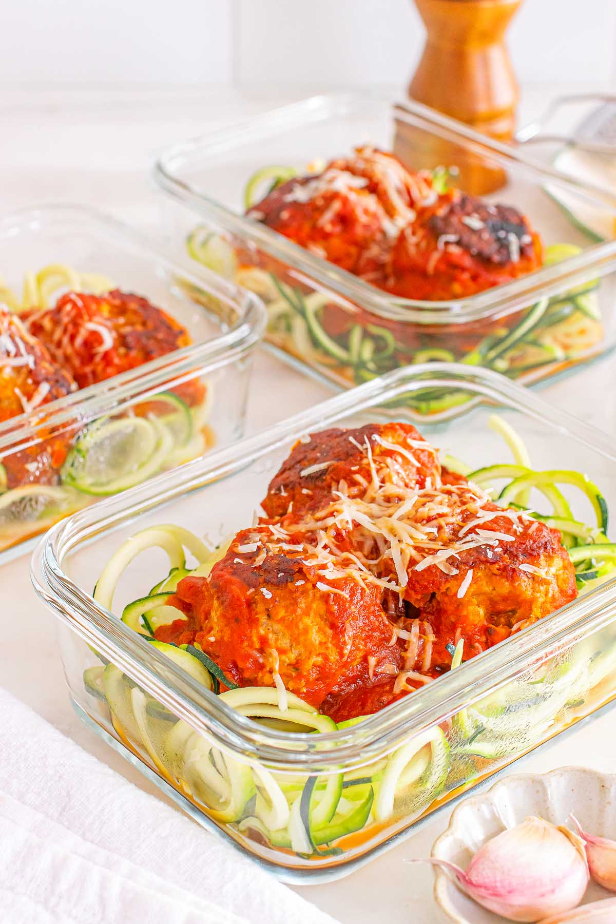 Glass containers with Meal Prep Turkey Meatballs & Zoodles in tomato sauce, topped with shredded cheese.