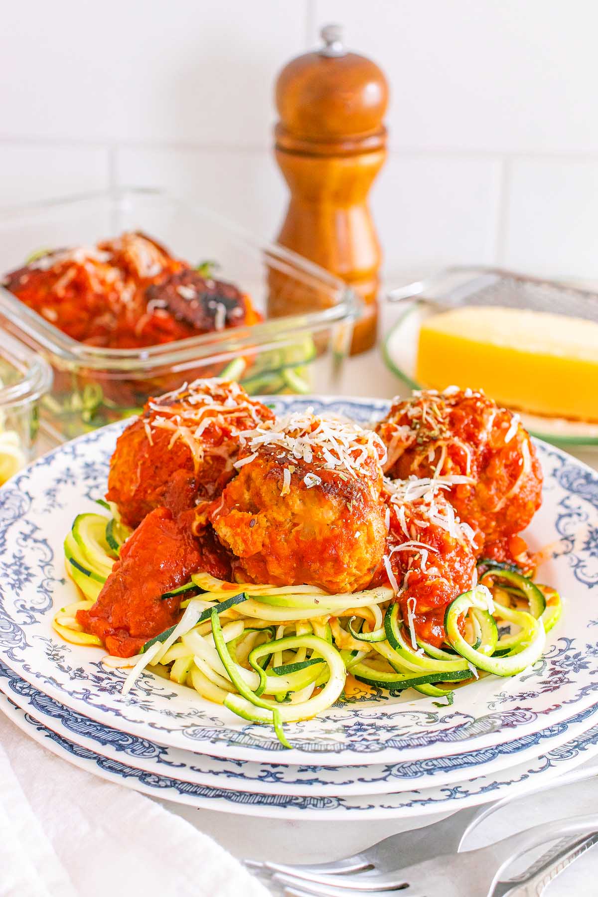 Meal Prep Turkey Meatballs & Zoodles in marinara sauce served over zucchini noodles on a patterned plate, topped with grated cheese.