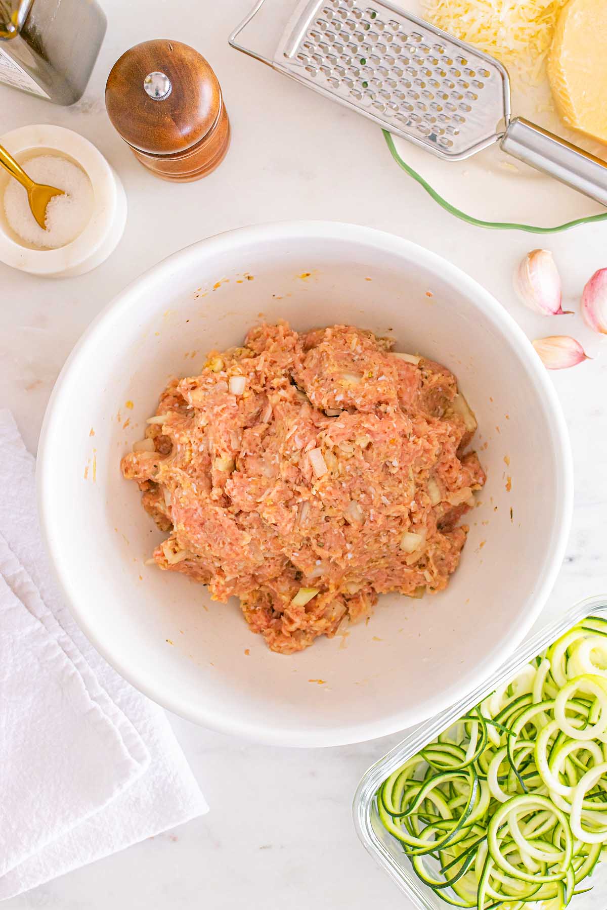 Raw meat mixture with chopped onions in a white bowl, surrounded by zucchini noodles and kitchen utensils—perfect for Meal Prep Turkey Meatballs & Zoodles.