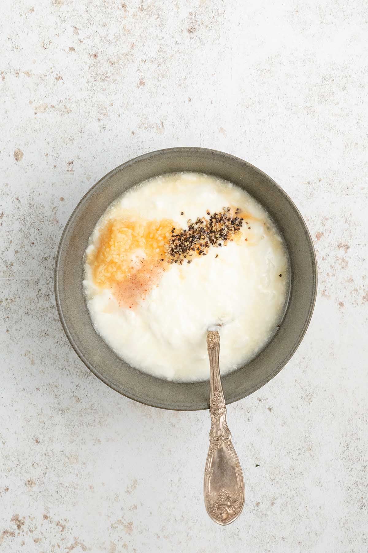 A bowl of yogurt with honey, black pepper, and cinnamon, served with a spoon on a light surface&mdash;perfect as a refreshing dip alongside spicy beef kofta.