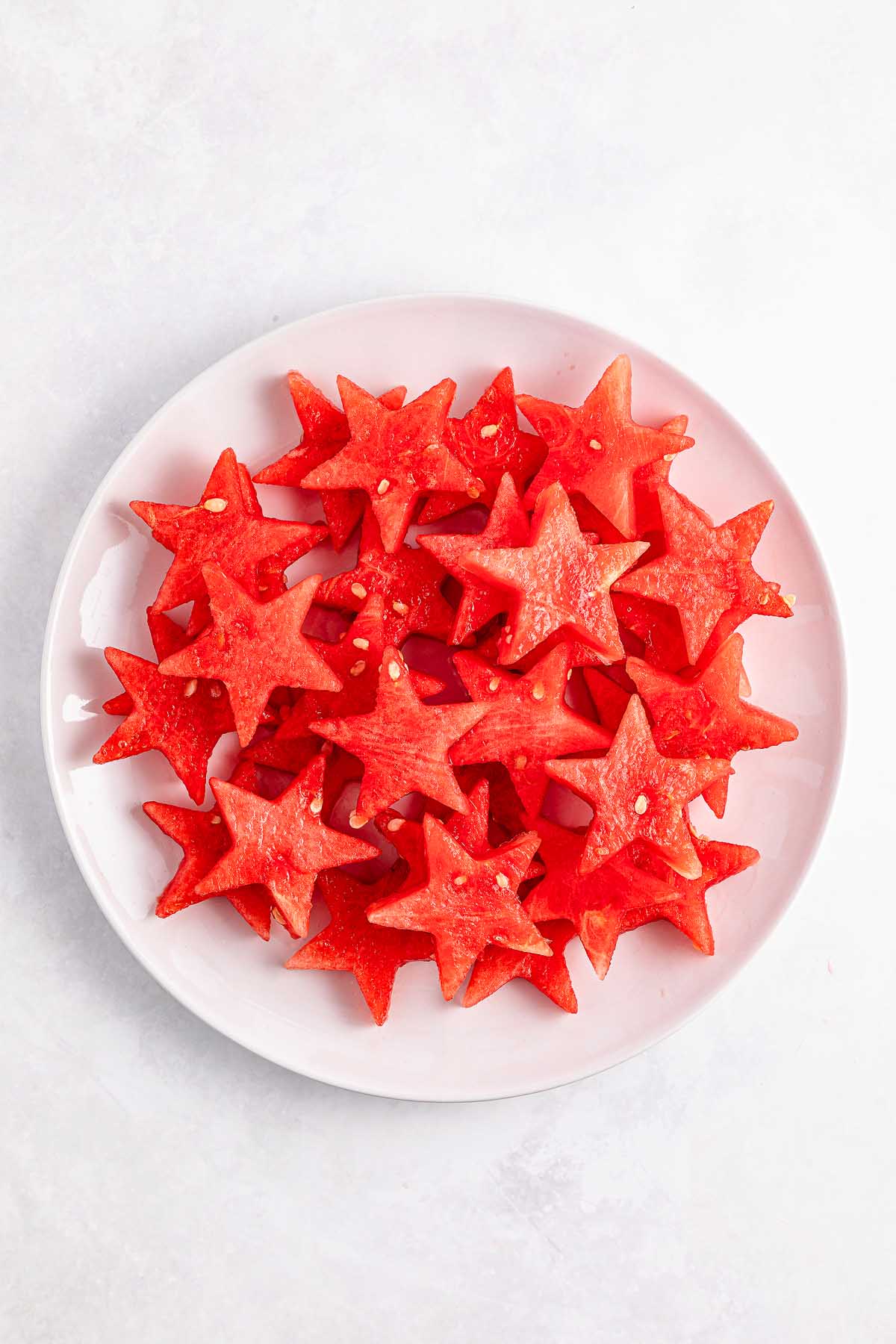 A white plate filled with star-shaped watermelon slices creates a festive display reminiscent of Watermelon Blueberry Sparklers on a light background.