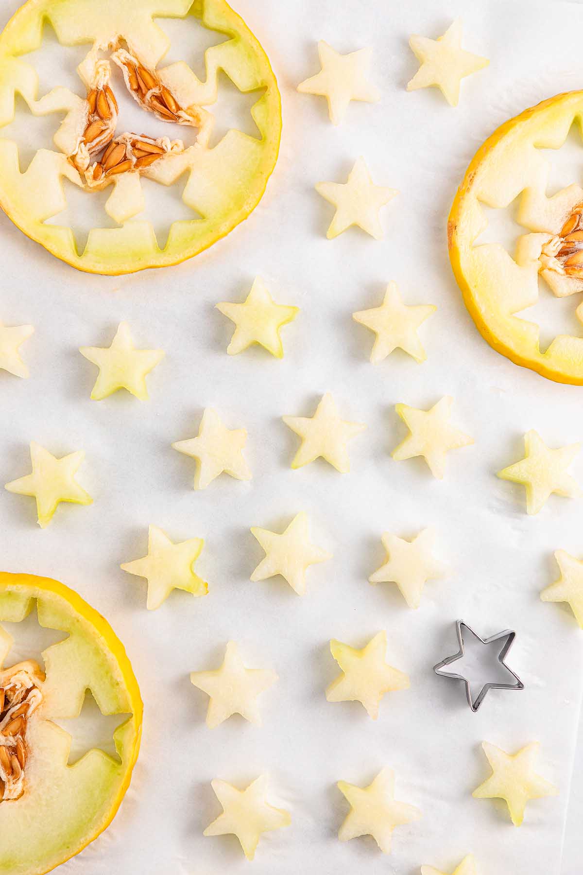 Slices of melon and small star-shaped pieces, perfect for making Watermelon Blueberry Sparklers, arranged with a star cookie cutter on a white surface.