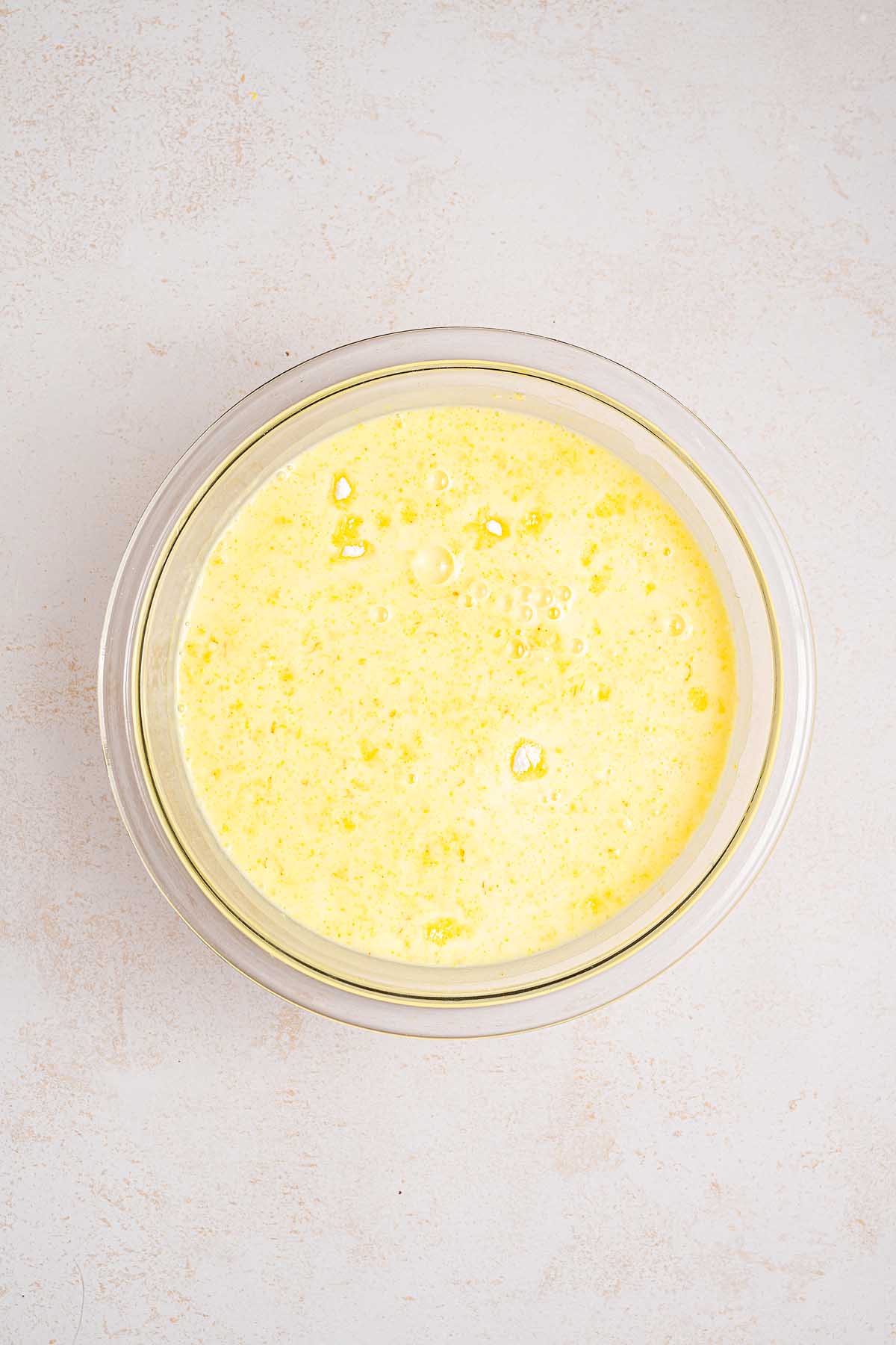 A glass bowl filled with a frothy, pale yellow lemon lush mixture sits on a light-colored surface.
