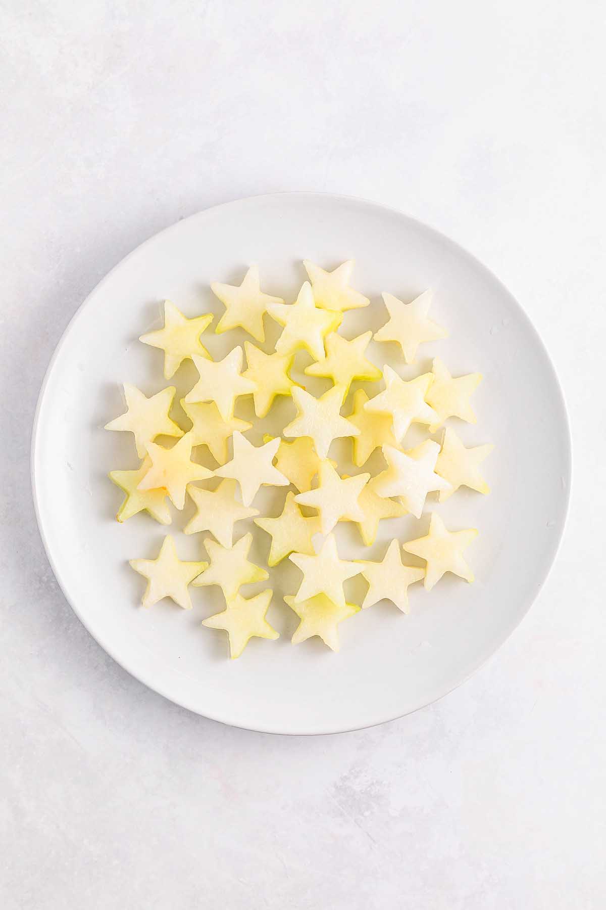 White plate with star-shaped apple slices and Watermelon Blueberry Sparklers arranged on it, on a light background.