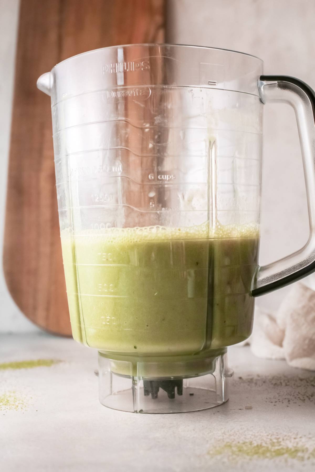 A blender jar filled with green smoothie with almond milk sits on a light countertop.
