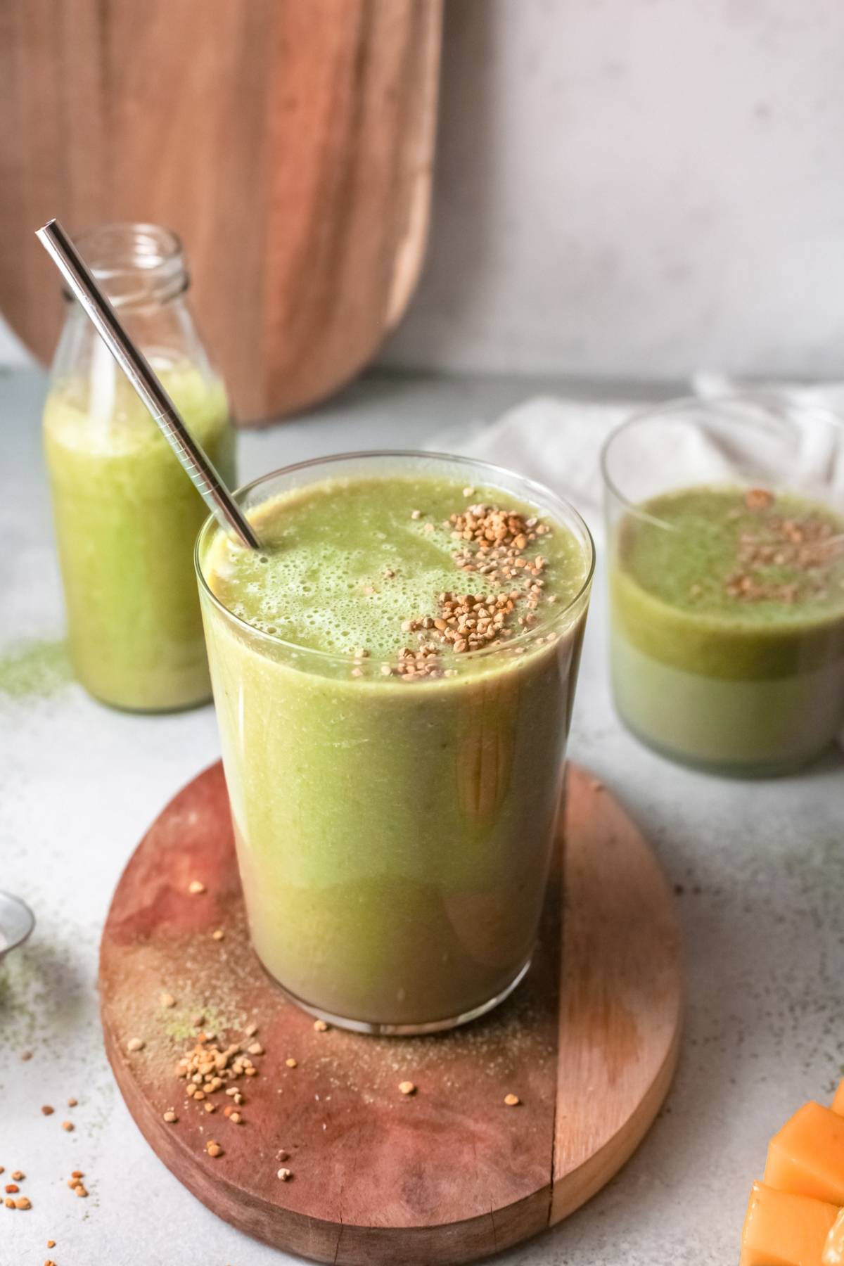 A glass of Mango Matcha Smoothie with a metal straw and sprinkled toppings sits on a wooden board, blending vibrant flavors into a refreshing treat.