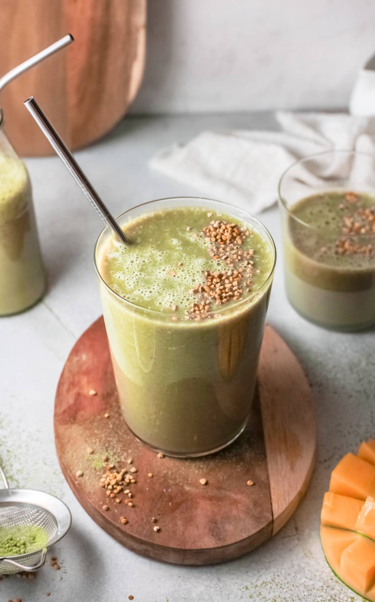 A glass of green mango smoothie with a metal straw and sprinkled seeds on top, placed on a wooden board—perfect for trying out a refreshing vegan smoothie recipe.