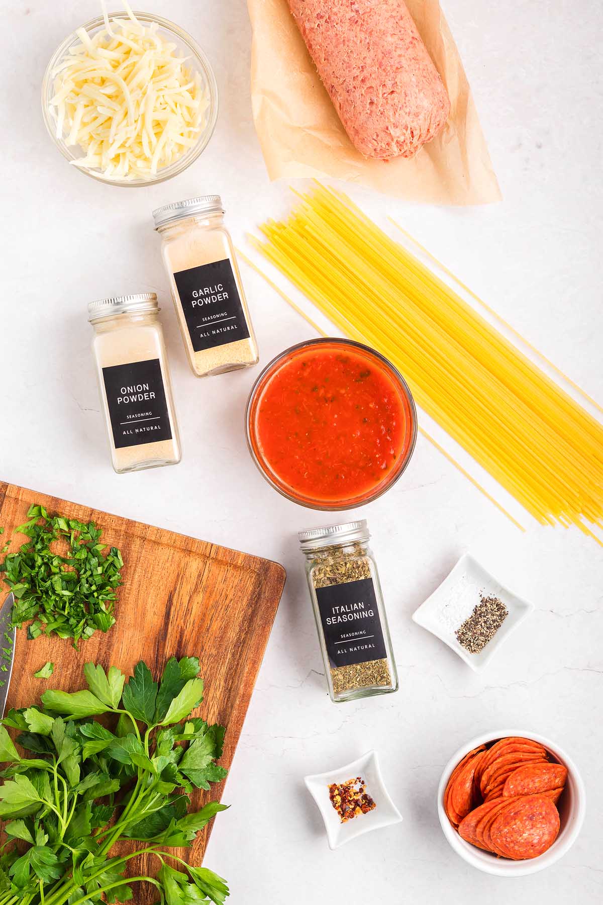 Ingredients for a spaghetti pizza dish: ground meat, spaghetti, cheese, spices, sauce, pepperoni, and fresh herbs.