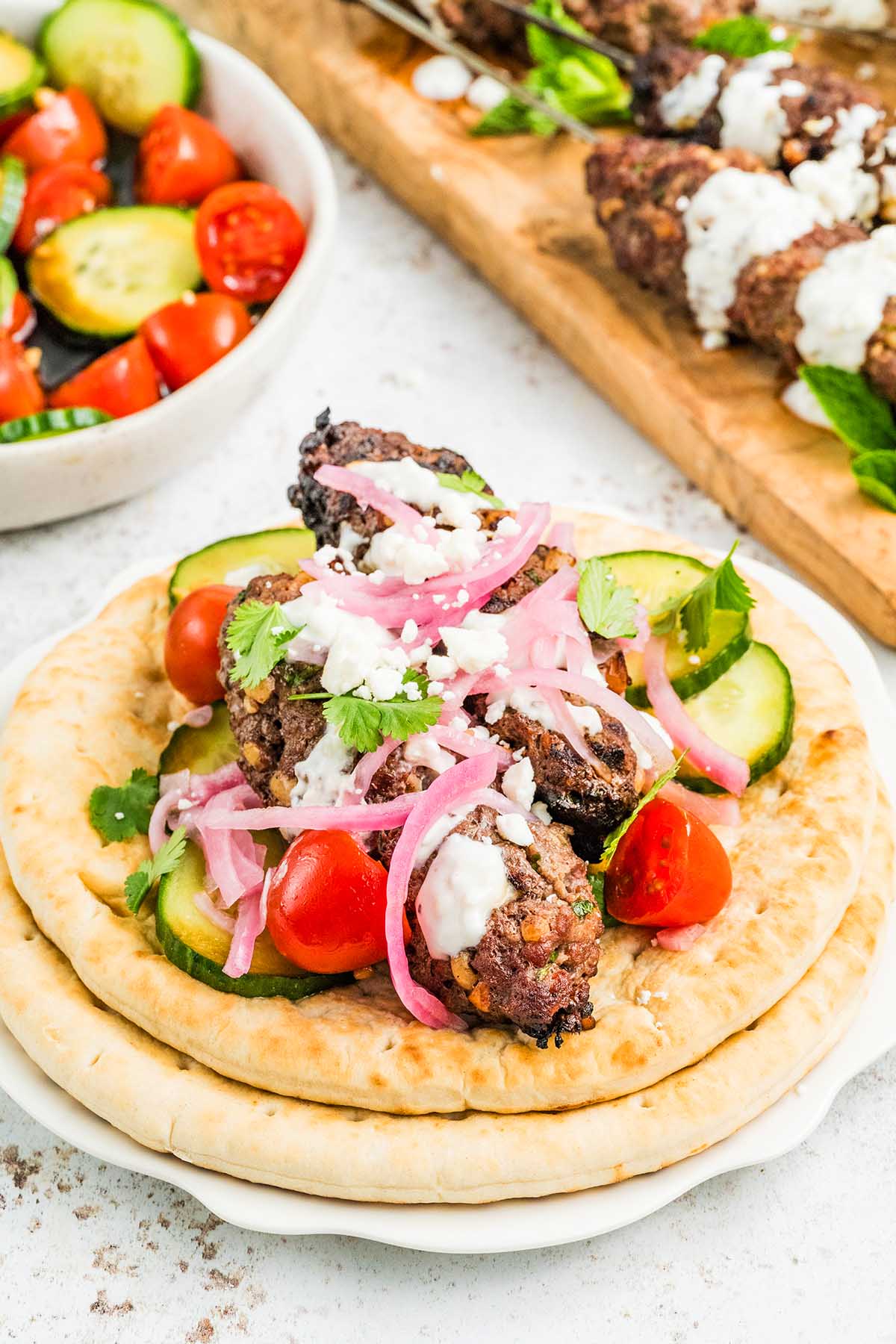 Pita bread topped with savory beef kofta, grilled meat, cucumbers, tomatoes, pickled onions, herbs, and crumbled cheese.