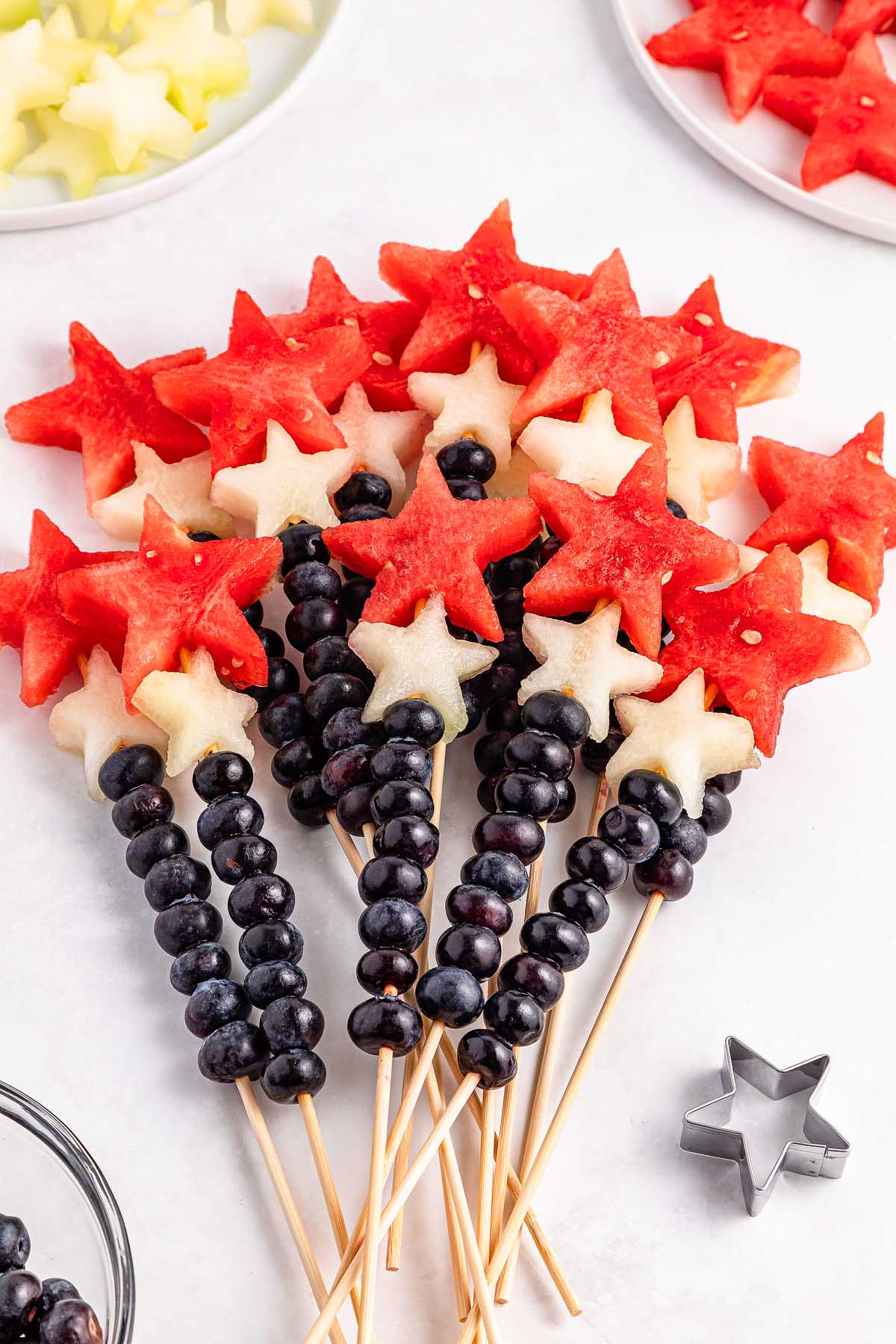 Watermelon Blueberry Sparklers skewers feature blueberries and star-shaped watermelon and melon pieces arranged like festive wands.