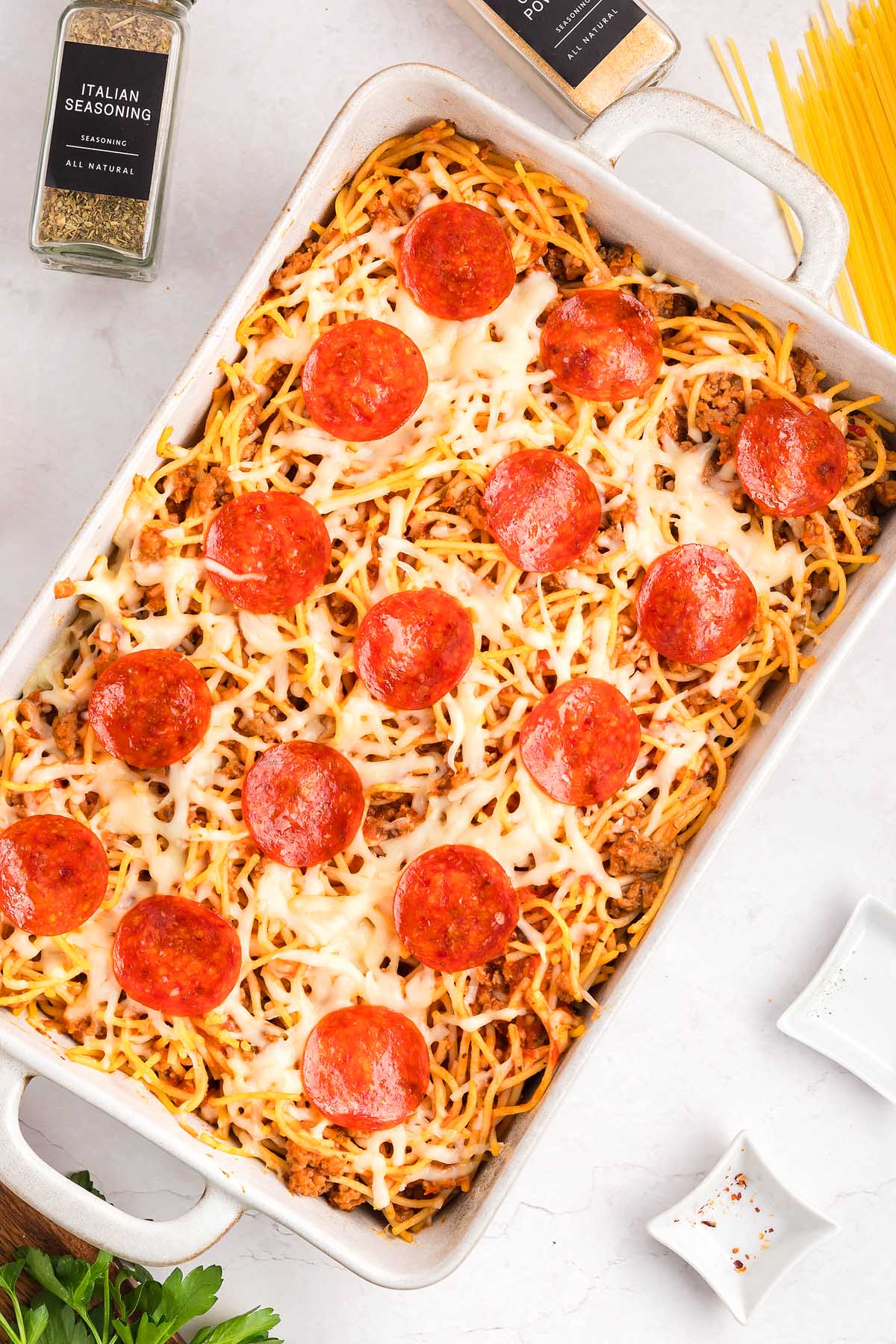 Baked spaghetti pizza casserole topped with melted cheese and pepperoni slices in a white rectangular dish.