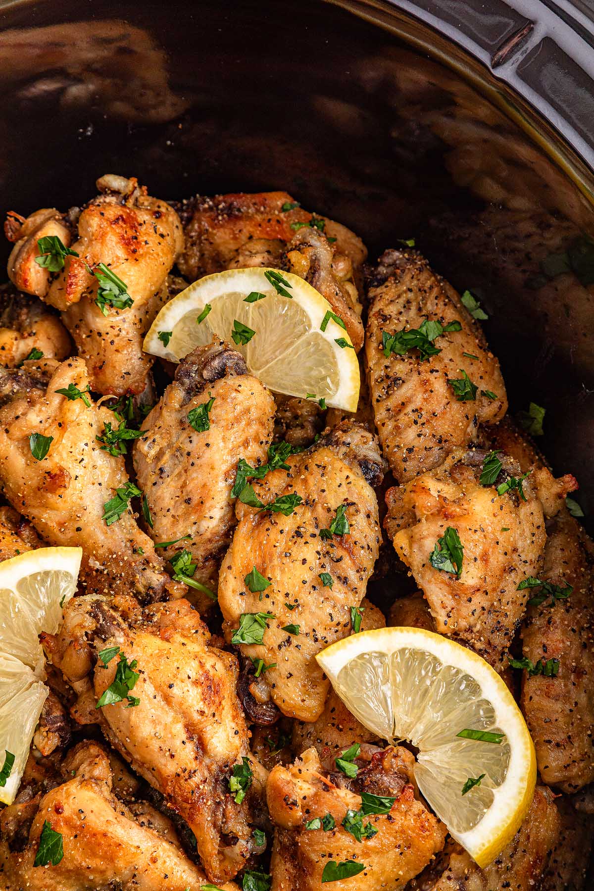 Close-up of slow cooker lemon pepper wings, garnished with fresh lemon slices and chopped parsley for a zesty finish.