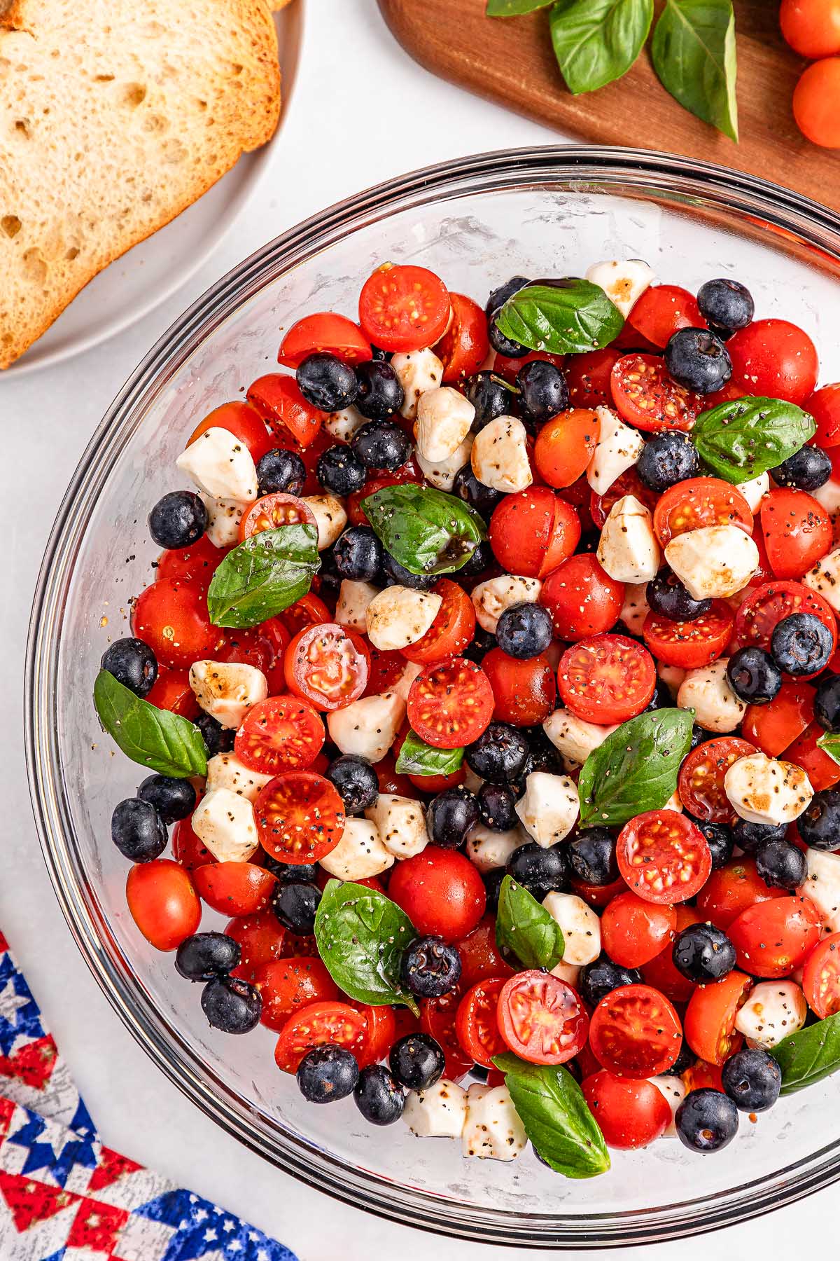 A bowl of blueberry tomato Caprese salad featuring cherry tomatoes, mozzarella, fresh blueberries, and basil leaves.