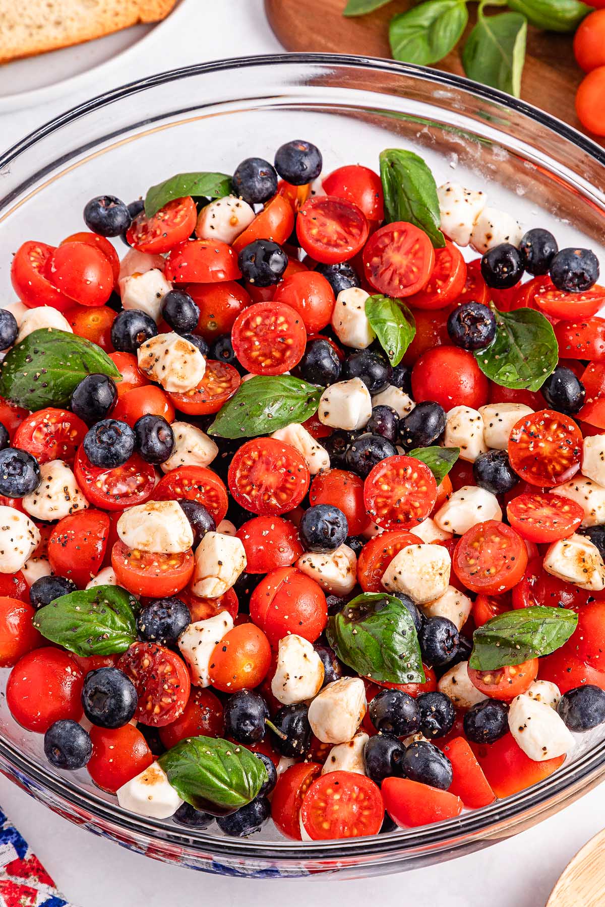A bowl of blueberry tomato Caprese salad with cherry tomatoes, blueberries, mozzarella balls, and fresh basil leaves.