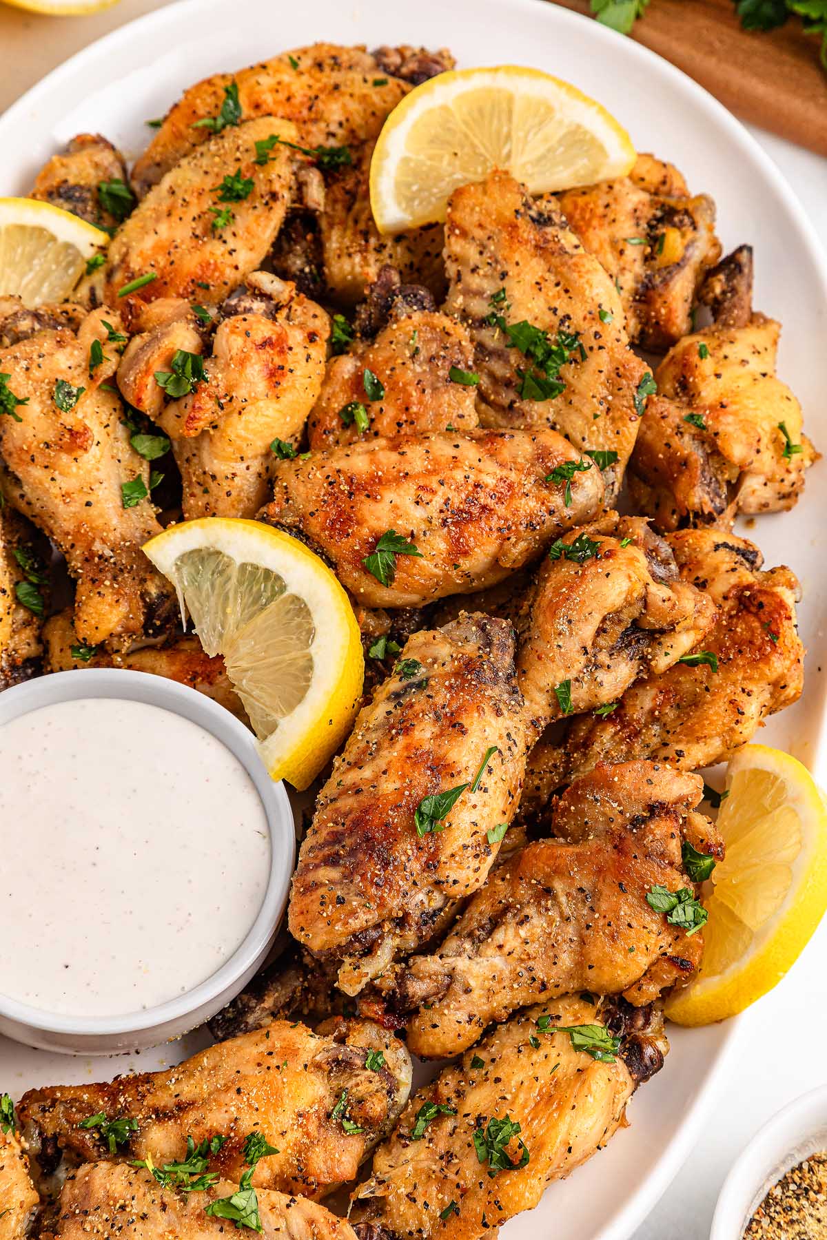 A plate of slow cooker lemon pepper wings garnished with lemon slices and parsley, served with a cup of dipping sauce.