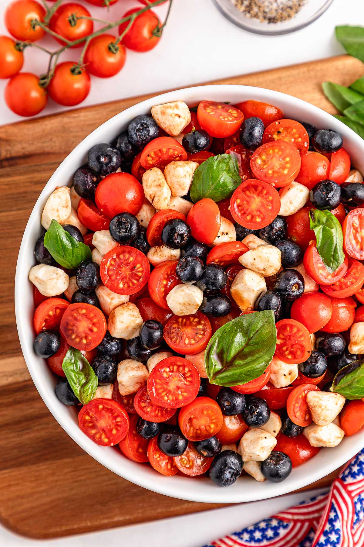 A bowl of blueberry tomato Caprese salad featuring cherry tomatoes, mozzarella balls, blueberries, and fresh basil leaves.