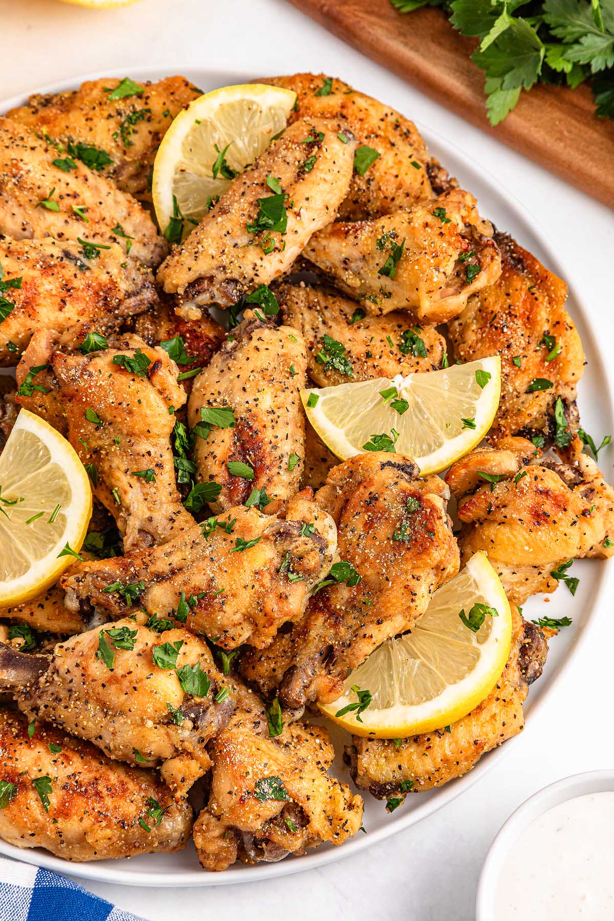 A plate of slow cooker lemon pepper wings, garnished with lemon wedges and chopped parsley.