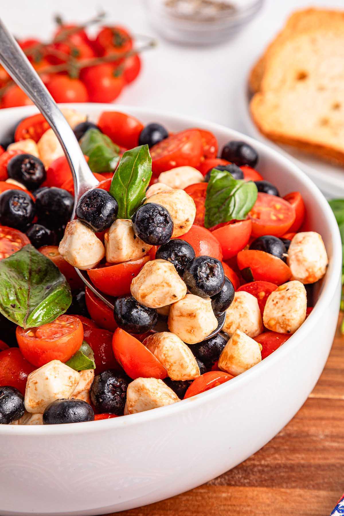 A bowl of blueberry tomato Caprese salad with cherry tomatoes, mozzarella balls, juicy blueberries, and fresh basil leaves.
