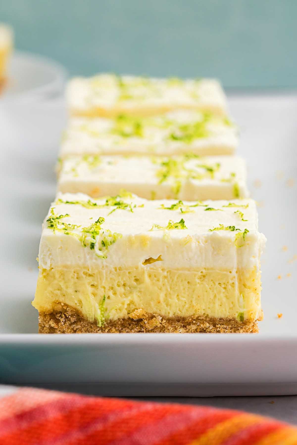 A close-up of creamy key lime bars topped with whipped cream and a sprinkle of lime zest, served on a white plate.