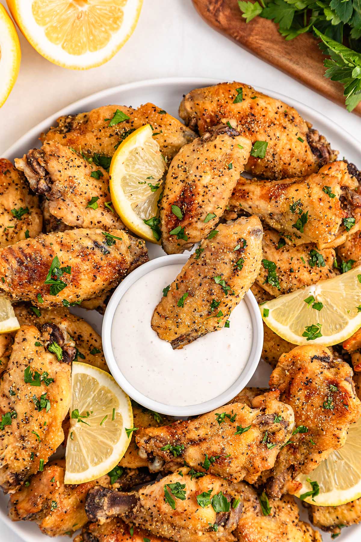 A plate of slow cooker lemon pepper wings with lemon slices and ranch dip, garnished with chopped parsley.