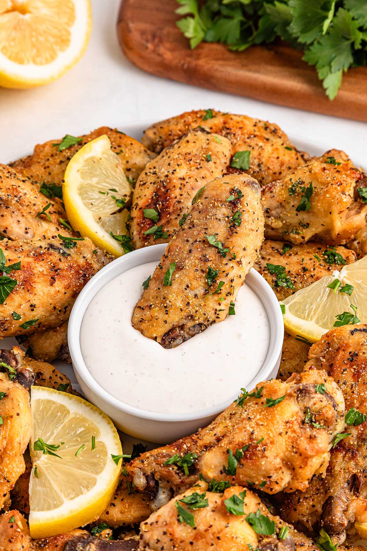 A plate of slow cooker lemon pepper wings is served with lemon slices and a bowl of dipping sauce in the center.