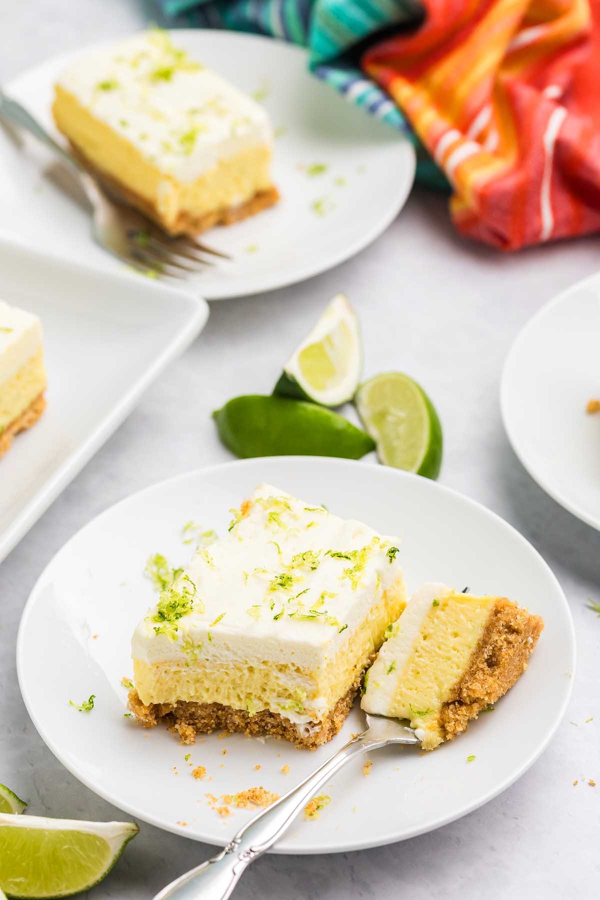 A plate with a slice of creamy key lime bar on a graham crust, topped with lime zest, and a forkful taken out.
