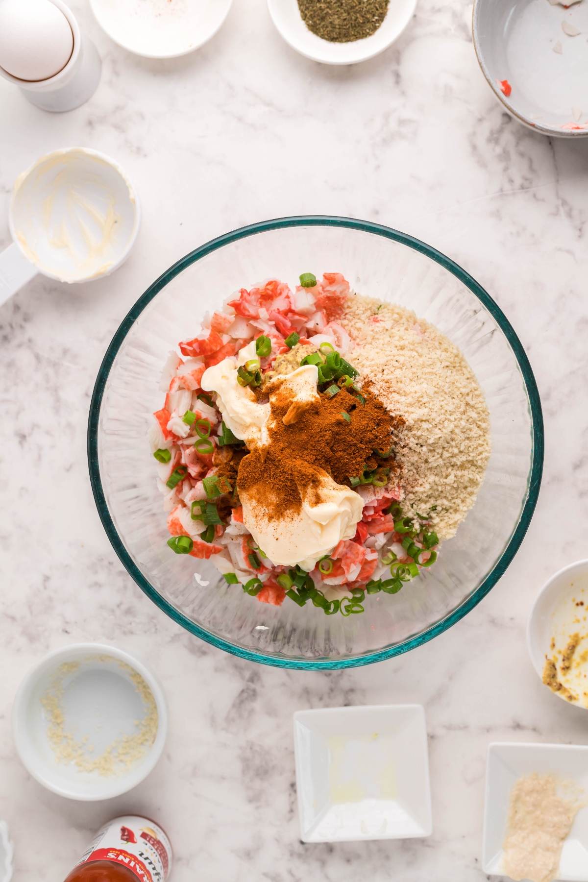Glass bowl with diced tomatoes, green onions, mayo, breadcrumbs, and spices—perfect ingredients for southwest crab cakes or for making delicious Air Fryer Crab Cakes on a marble countertop.