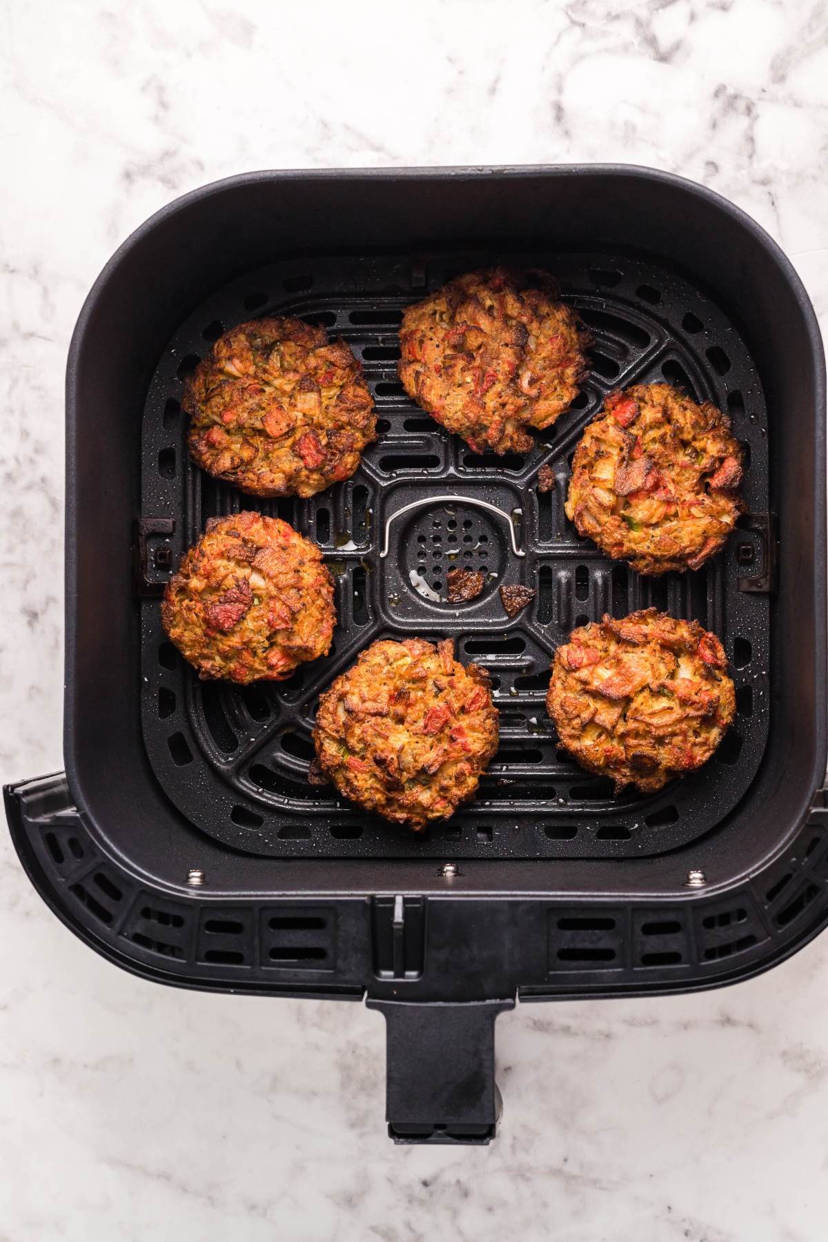 Six veggie patties arranged in an air fryer basket on a white marble countertop, similar to how you’d prepare Air Fryer Crab Cakes for a delicious, crispy texture.