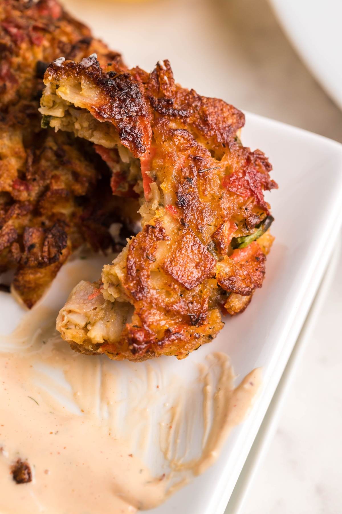 Closeup of a crispy southwest crab cake with a bite taken out, served on a white plate with creamy spicy sauce for crab cakes.