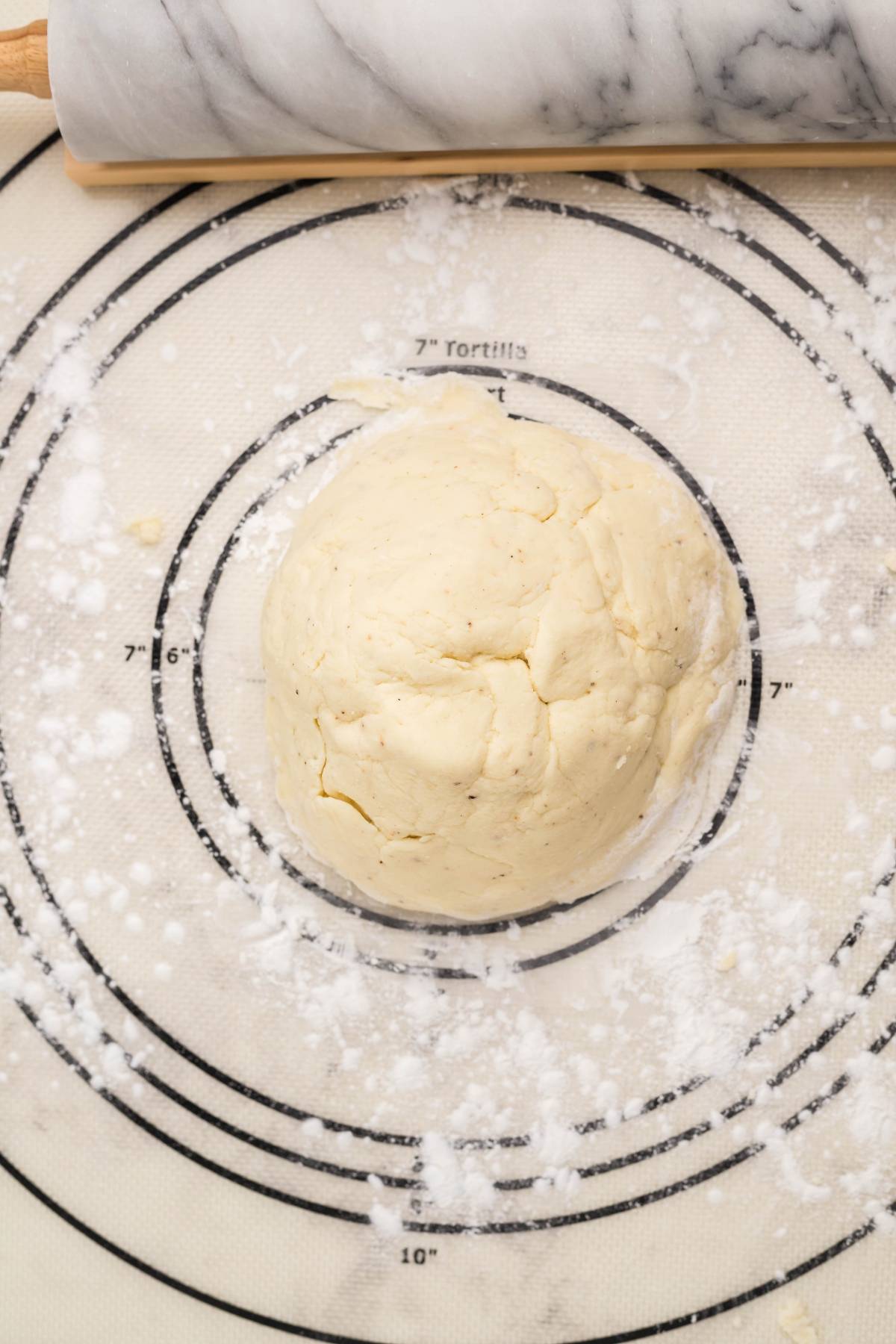 Ball of dough on a floured pastry mat with measurement rings, next to a marble rolling pin—perfect for making easy gluten free egg rolls or trying your favorite air fryer egg rolls recipe.