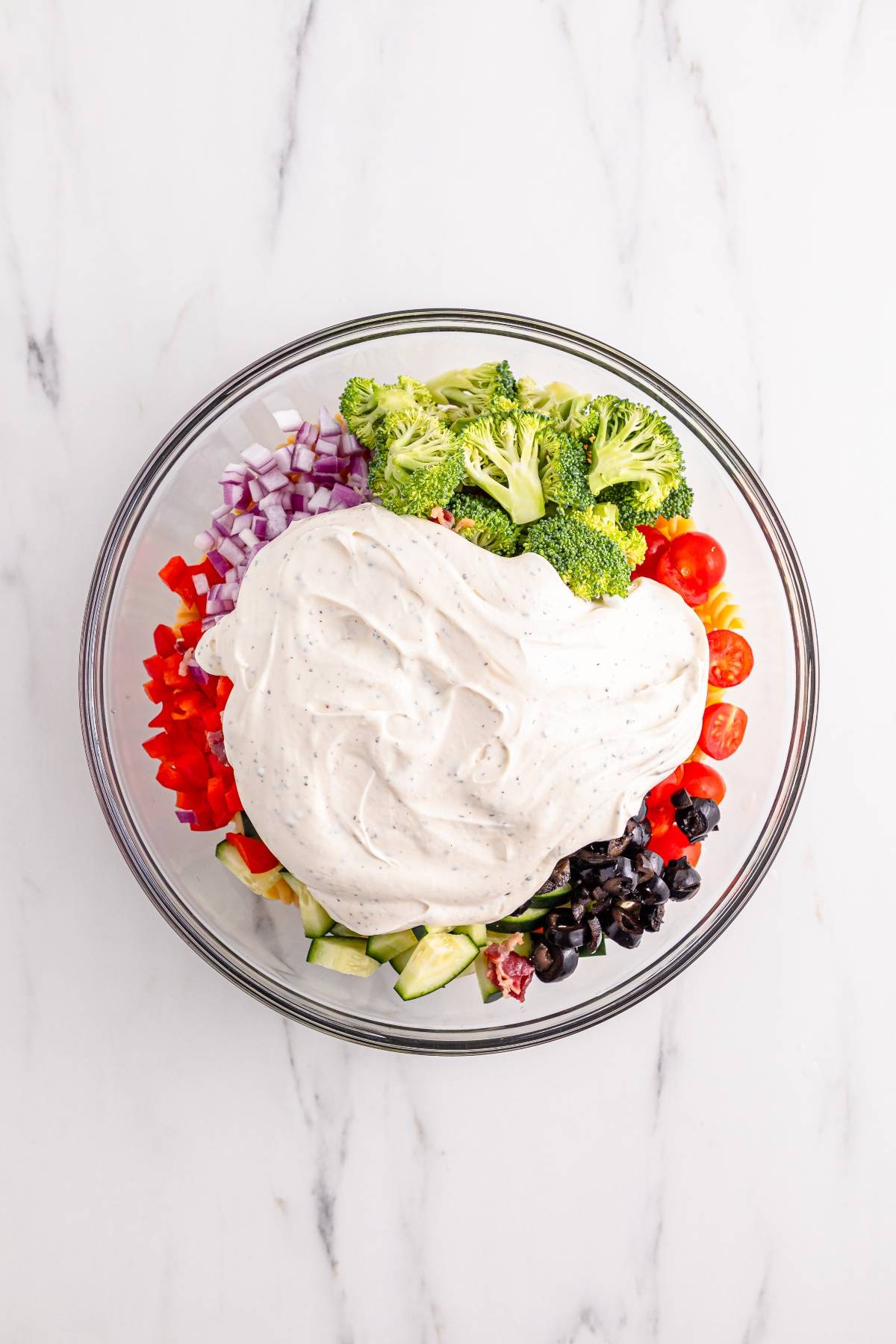 Bowl with chopped veggies, olives, and a large dollop of creamy dressing on top, viewed from above.