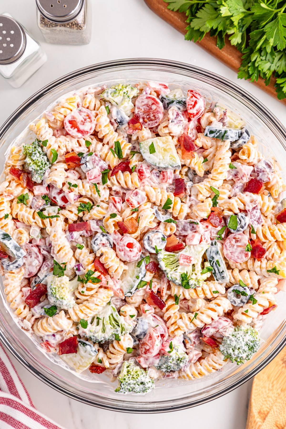 Pasta salad with rotini, broccoli, tomatoes, bacon, and creamy dressing in a glass bowl, garnished with parsley.