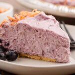 A slice of creamy blueberry cream pie on a plate, served with fresh blueberries and a fork.