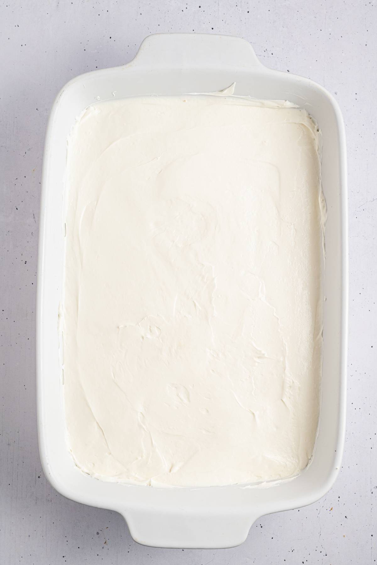 A white rectangular baking dish filled with a smooth layer of creamy white mixture.
