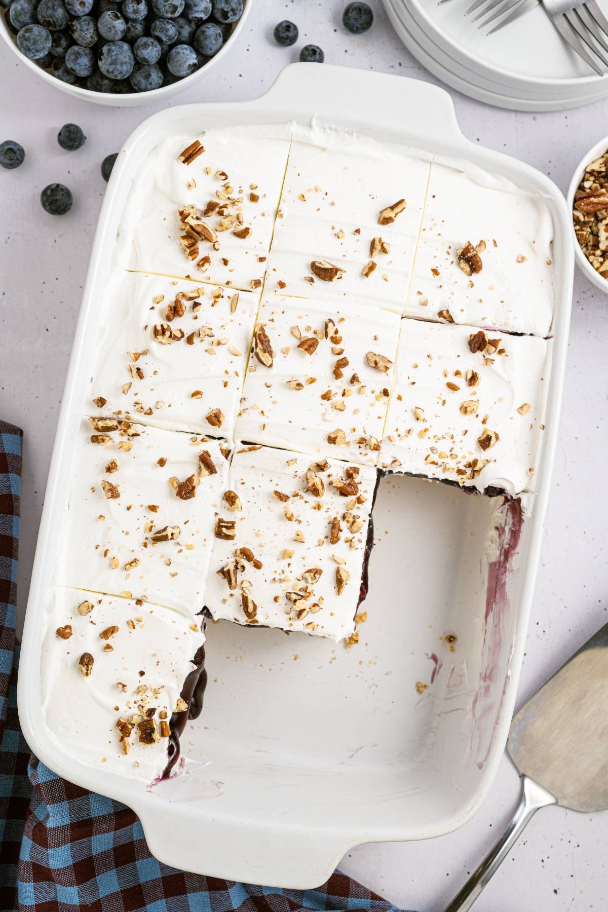 Rectangular dish with whipped cream-topped dessert, cut into squares, sprinkled with chopped nuts.