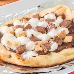 A campfire s'mores pizza featuring flatbread topped with chocolate, marshmallows, and graham cracker pieces on foil.