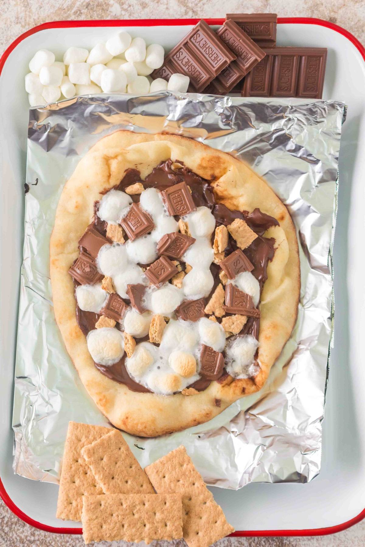 Naan on foil topped with melted chocolate, marshmallows, and graham crackers, with ingredients on the side.