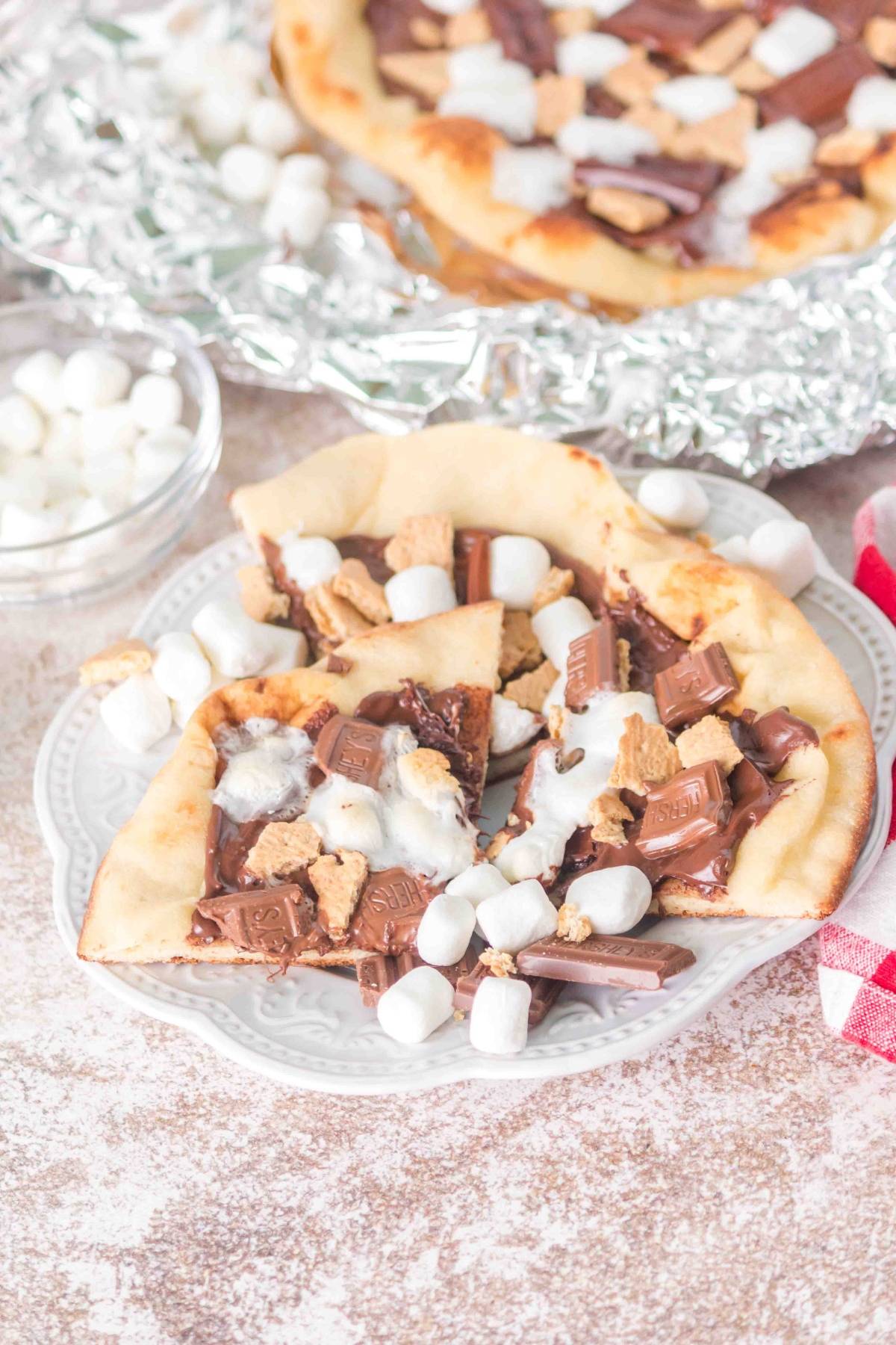 Naan pizza topped with melted chocolate, mini marshmallows, and graham cracker pieces on a white plate.
